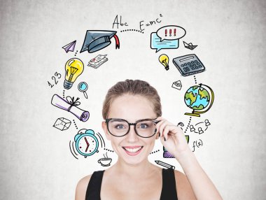 Gözlüklerini dokunmaktan ve kameraya bakarak neşeli bir genç kadın portresi. Siyah kolsuz bluz ve uzun saçları at kuyruğu ya da topuz. Renkli eğitim simgeler beton duvara çizilen bir daire içinde.