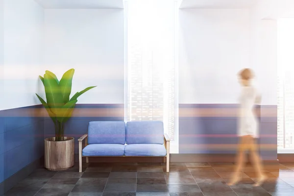 Woman in a lobby of a white and blue spa with a tiled floor, a blue sofa and a potted plant in the corner. 3d rendering mock up toned image blurred