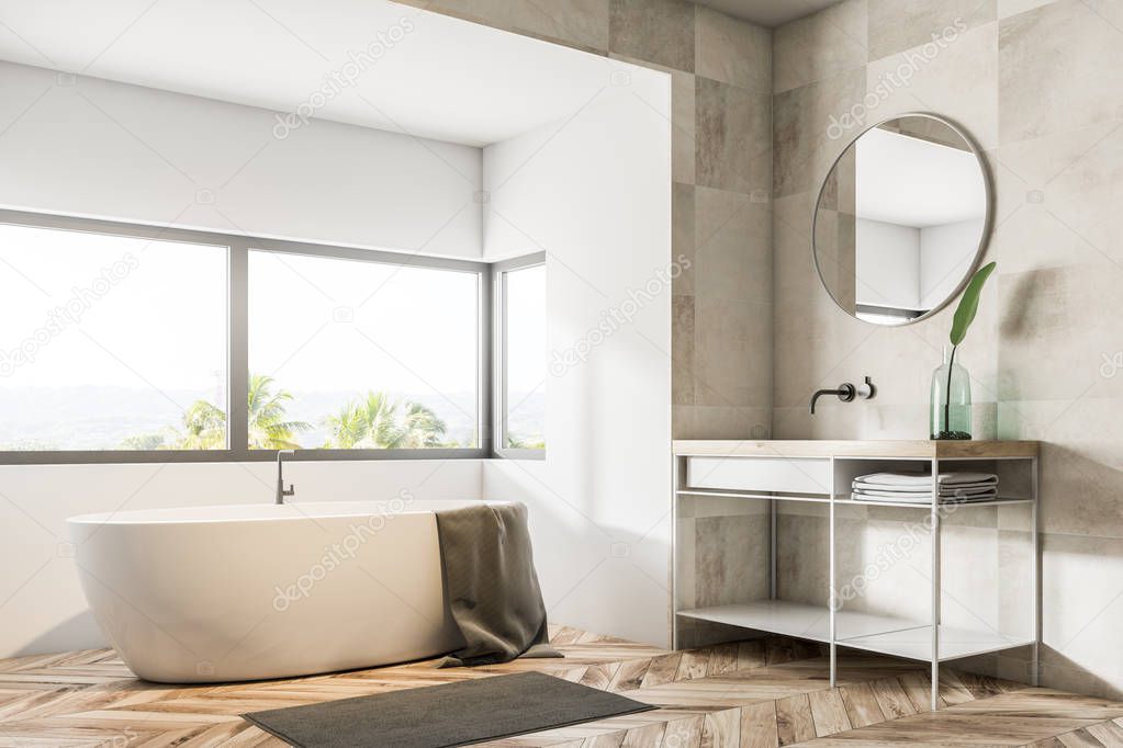 Bathroom corner with beige tile walls, a wooden floor, a bathtub under a large window, a sink and a round mirror. 3d rendering