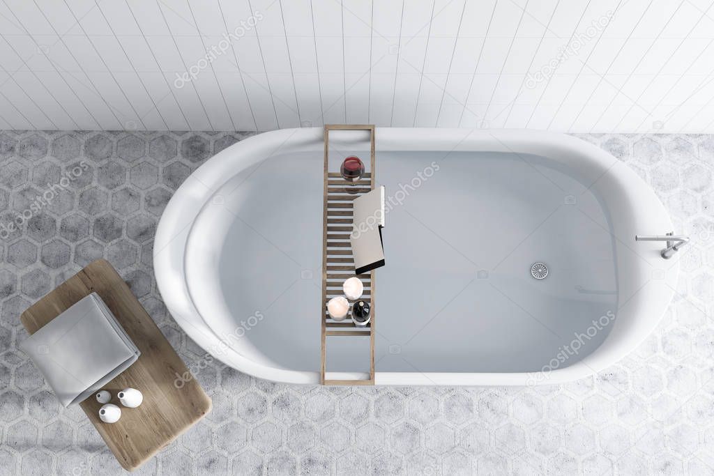 Elegant white bathtub filled with water standing in a luxury bathroom interior with white tiled walls, and a hexagon tile floor. A mock up open book on a shelf. 3d rendering top view