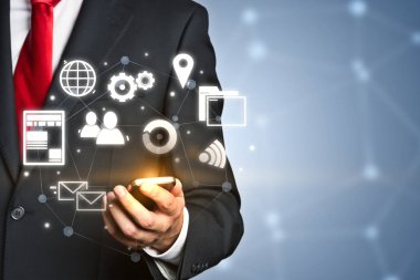 Takım elbise ve kravat smartphone tutarak ve kendi ekranına bakarak tanınmaz halde iş adamı. Gri arka plan bulanık ağ ile. İş ikonları/simgeleri ön plan arabirim. Tonlu görüntü pozlama sahte katlayın