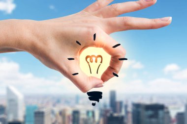 Kadın el Sarı parlak içinde bulanık şehir arka plan üzerinde çizilmiş ampul ile ok işaretiyle gösterilen. Fikir kavramı