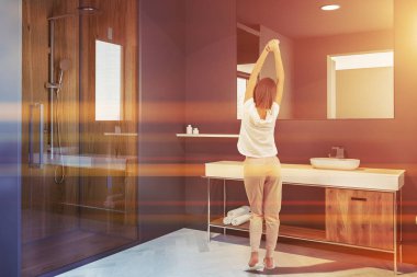 İskandinav tarzı banyo köşedeki Gri duvarlar, beyaz bir ahşap zemin, bir lavabo ve bir tahta sandalyede yukarıda büyük bir ayna ile bir kadın. Cam kapı duş. 3D render sahte tonlu görüntü