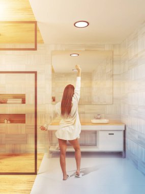 Kadının yanına bir beyaz tahta duvarda asılı dikey bir ayna ile bir banyo lavabo. Cam duş kabini sola. 3D render tonlu görüntü