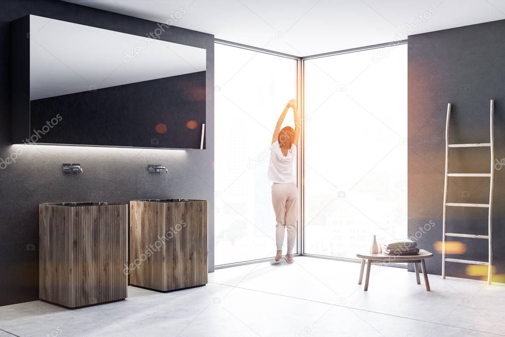 Woman in pajamas near wooden double sink with a long horizontal mirror hanging above it in a luxury black wall loft bathroom interior. Spa Hotel. Ladder and table. 3d rendering mock up toned image