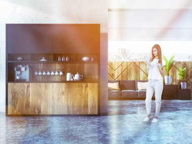 Genç kadın ile studio apartment ile mutfak köşesi ve gri rahat kanepe yastıkları ile smartphone. 3D render tonlu görüntü