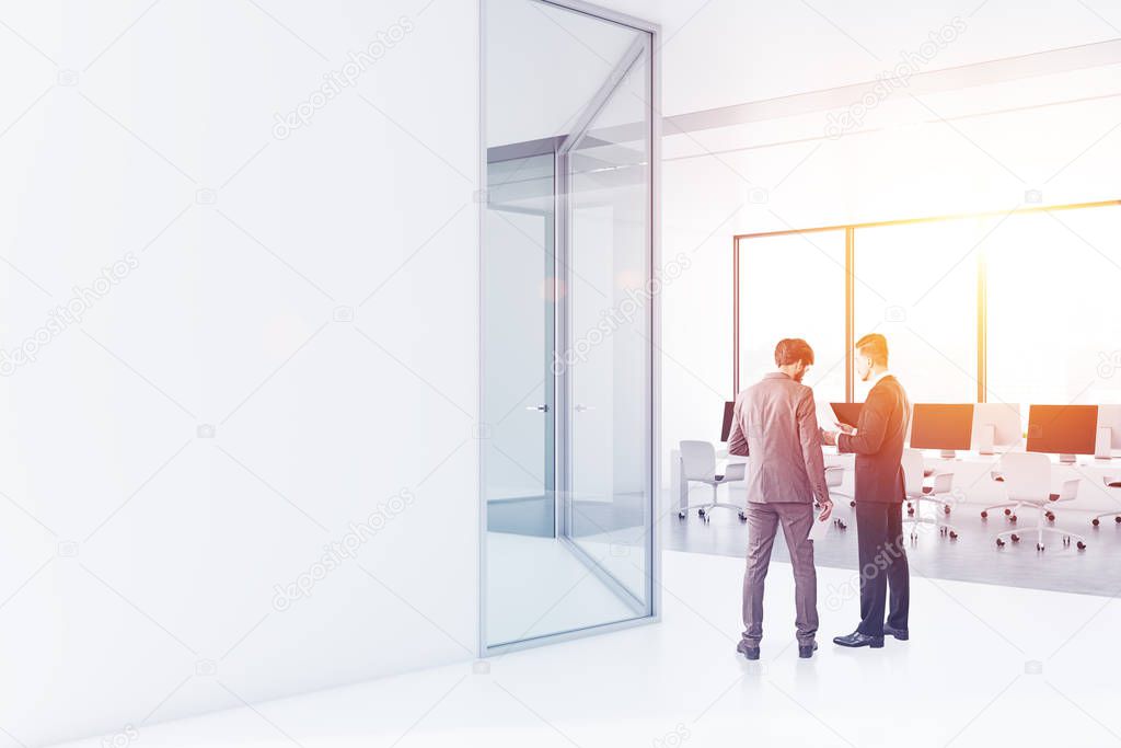 Two business partners talking in a white office hall with panoramic windows, white walls and open space area with computer tables. Copy space wall Toned image