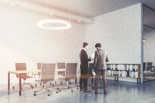 Two businessmen talking in Industrial style board room interior with concrete walls and floor, a wooden table and metal chairs. Round ceiling lamp and pipes. Toned image