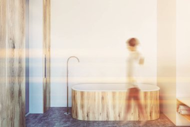 Beyaz duvarlar, beton zemin ve ahşap küvet lüks banyo iç. Dikey ayna. Yürüyen genç kadın. Görüntü bulanık tonda