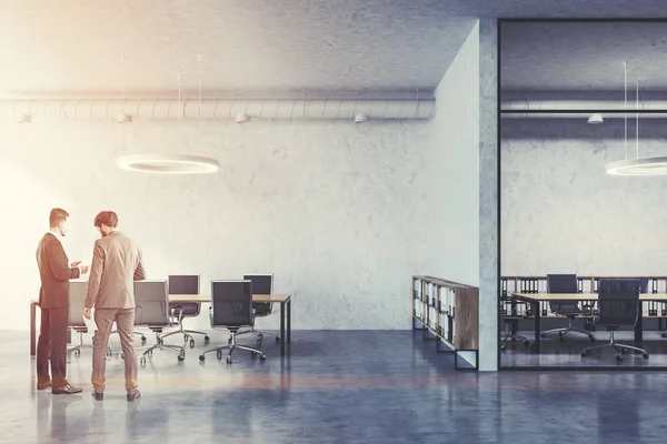 Two business partners discussing company issues in interior of industrial style conference room with concrete and glass walls, two wooden tables and metal chairs. Toned image