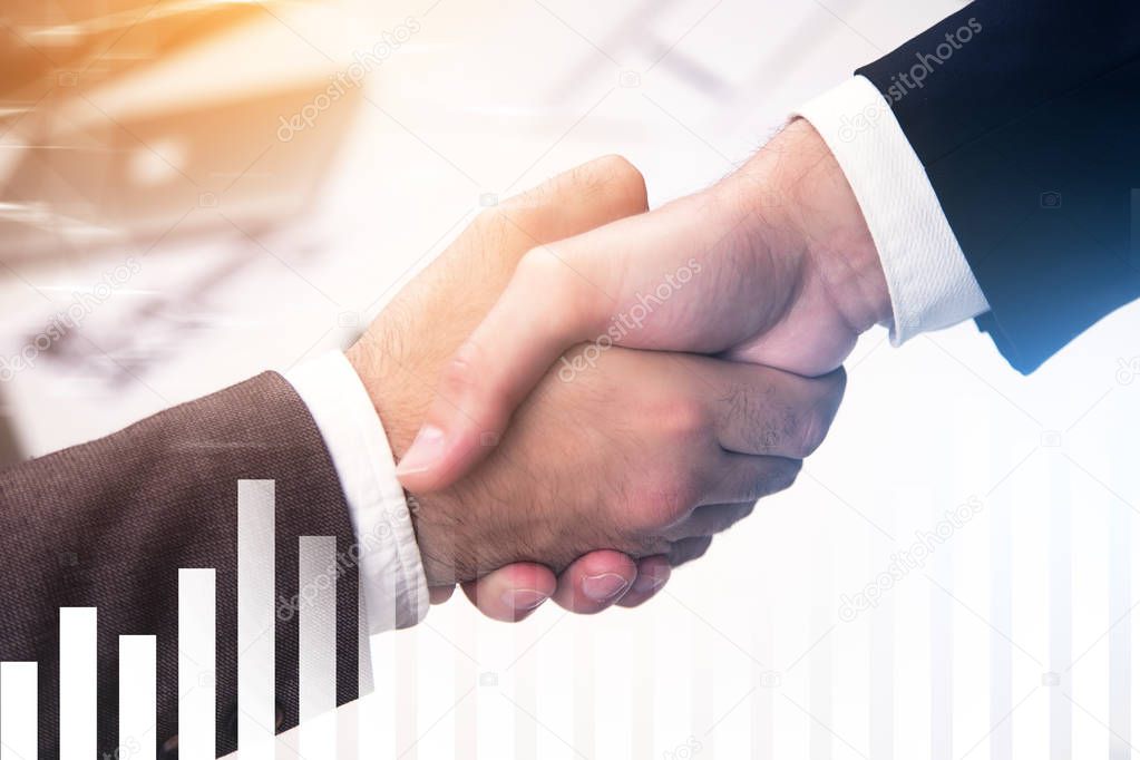 Close up of two businessmen shaking hands over a blurred office background. Graphs and diagrams in the foreground. Sealing a deal concept. Toned image double exposure
