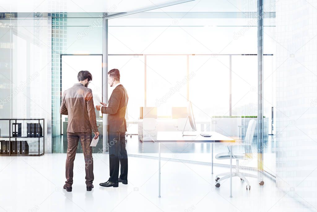 Two businessmen talking in manager office with white walls and floor, gray table with computer on it. Shelves with folders and open plan office in the background. Toned image double exposure