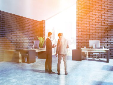 İki iş ortağı ofislerine siyah tuğla duvarlar ve büyük pencere ile konuşan. Danışmanlık şirketi kavramı. Tonlu görüntü