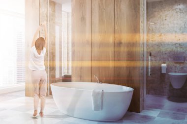 Yan görünüm ahşap duvarlar, beyaz lüks banyo fayans zemin ve beyaz küvet. Dikey ayna ve bir tuvalet. Genç Kadın pijama. Tonlu görüntü