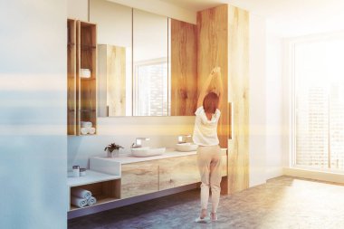 Lüks çatı banyo ahşap duvarlar, ahşap ve siyah tezgah üzerinde duran siyah çift lavabo ile köşesine Rulo havlu ve kremler ile temizleyelim. Genç Kadın pijama. Tonlu görüntü