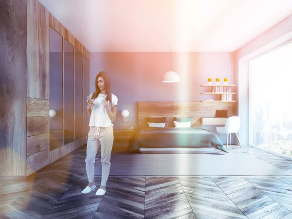 妇女与智能手机在室内的时尚卧室与蓝色墙壁 木地板 绿色主床和整齐的电脑桌在角落里 色调图像 — 图库照片