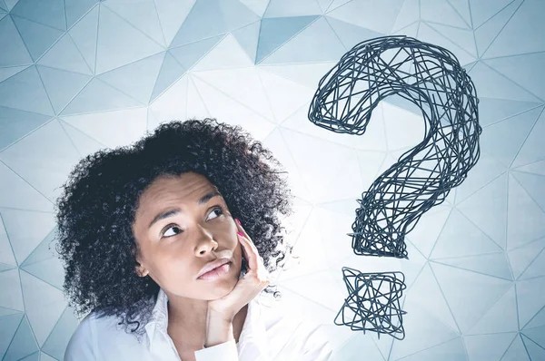 Portrait of thoughtful young african american woman with curly black hair looking up with her hand on the chin. Gray wall background with big question mark on it.