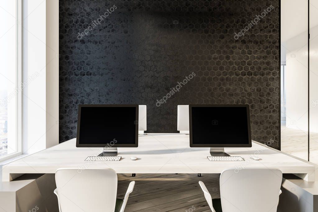 Black computer screens standing on white tables in minimalistic hexagon wall pattern office with wooden floor and loft windows. 3d rendering copy space