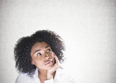 Elinde çene ile ararken kıvırcık siyah saçlı düşünceli genç Afro-Amerikan kadın portresi. Beton duvar arka plan. Karar verme kavramı. Yukarı alay