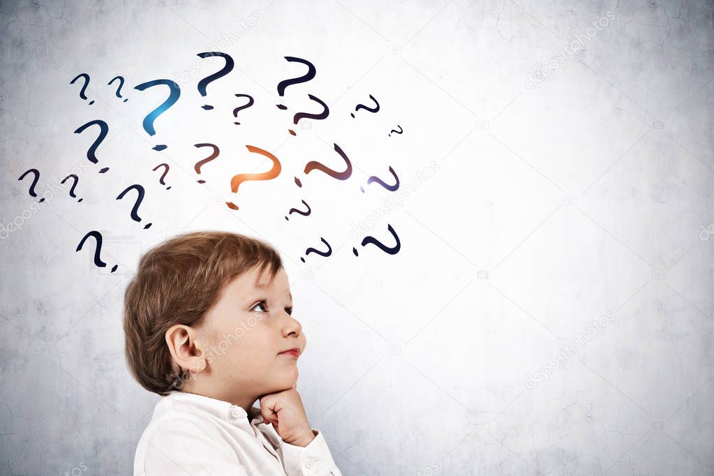 Adorable little boy in white shirt thinking standing near a gray wall with many question marks on it. Knowledge and seaking for answer concept. Mock up