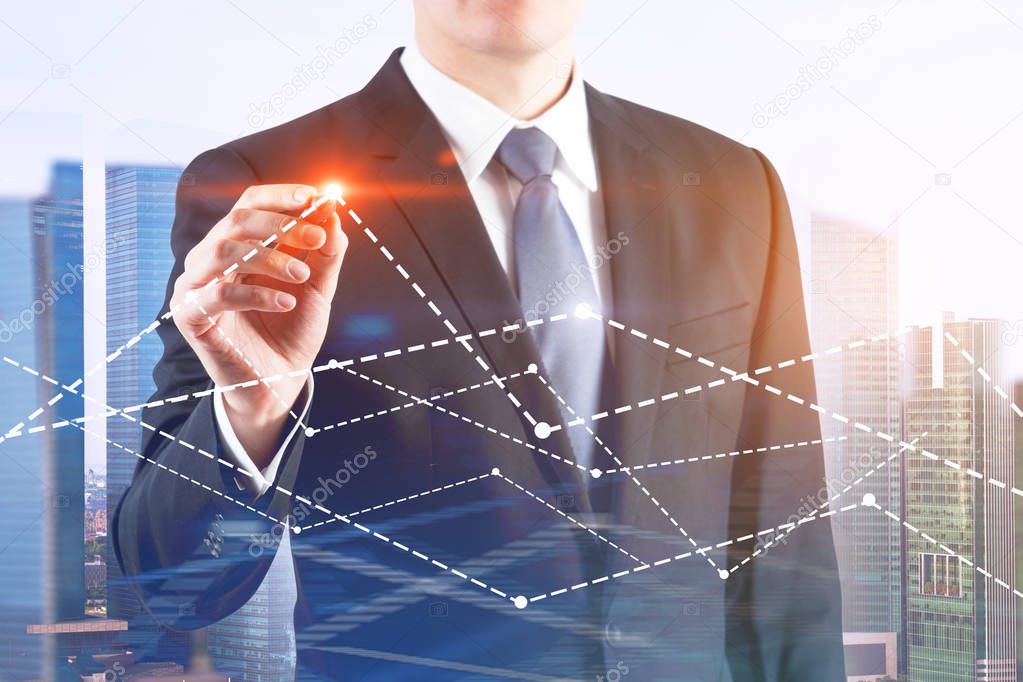 Unrecognizable young businessman drawing graphs with glowing pen. Modern cityscape background. Toned image double exposure