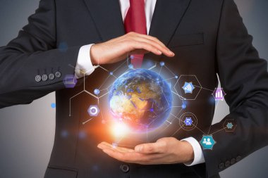 Siyah takım elbise ve kravat holding dünya hologram ve renkli Internet şeyler simgeler gri duvarının yakınında tanınmayan bir işadamı. Görüntü çift pozlama Nasa tarafından döşenmiş bu görüntü unsurları tonda