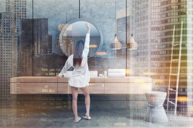 Banyo iç beton duvarlar ve zemin ve beyaz açısal Lavabonun üstündeki yuvarlak ayna ile ahşap tezgah üzerinde ayakta duran kadın. Merdiven köşede. Çift tonlu görüntü pozlaması