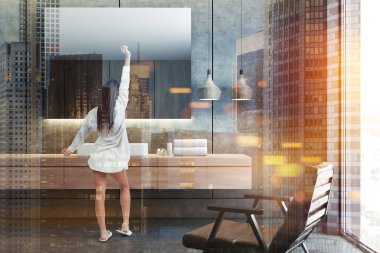 Yatay ayna üstünde cocnrete duvar banyoda asılı beyaz köşe lavabo ayakta ahşap tezgah üzerinde yakın duran kadın. Deri koltuk. Çift tonlu görüntü pozlaması