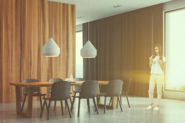 Duran beyaz ve ahşap duvarlar ile modern dining room, koyu gri sandalye ve büyük pencereler ile ahşap masa kadın. Tonlu görüntü