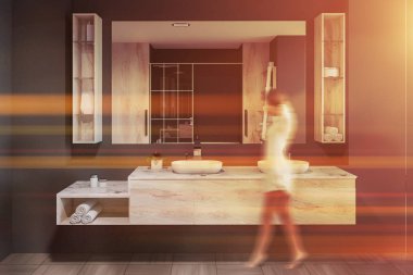 Modern banyo iç Gri duvarlar ile yürüyen kadın büyük ayna asılı üstündeki ile ahşap tezgah üzerinde zemin ve beyaz çift lavabo duran döşenir. Tonlu görüntü bulanık