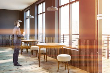 Gri duvarlar, ahşap zemin, modern kafe köşesinde ayakta işadamı ahşap masa ve pencere boyunca küçük yuvarlak sandalye yuvarlak. Tonlu görüntü