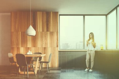 Kadın beyaz ve ahşap mutfak iç döşeme zemin, geniş pencere, gri mutfak tezgahı ve gri sandalye ile ahşap masa. Çift tonlu görüntü pozlaması