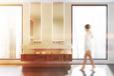 Yukarıda asılı iki dar aynalar ile çatı banyo iç beyaz duvarlar, beton zemin ve çift lavabo ile yürüyen kadın. Tonlu görüntü bulanık