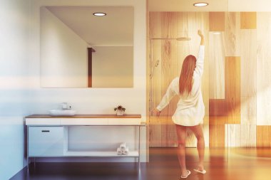 Modern banyo iç duvarlar, gri ve ahşap ile duran kadın büyük kare ayna ile lavabo ve duş kabini. Tonlu görüntü