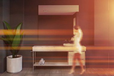 Modern banyo iç Gri duvarlar ile yürüyen kadın döşeli zemin ve beyaz lavabo üzerinde ahşap tezgah üstünde asılı büyük ayna ile ayakta. Tonlu görüntü bulanık