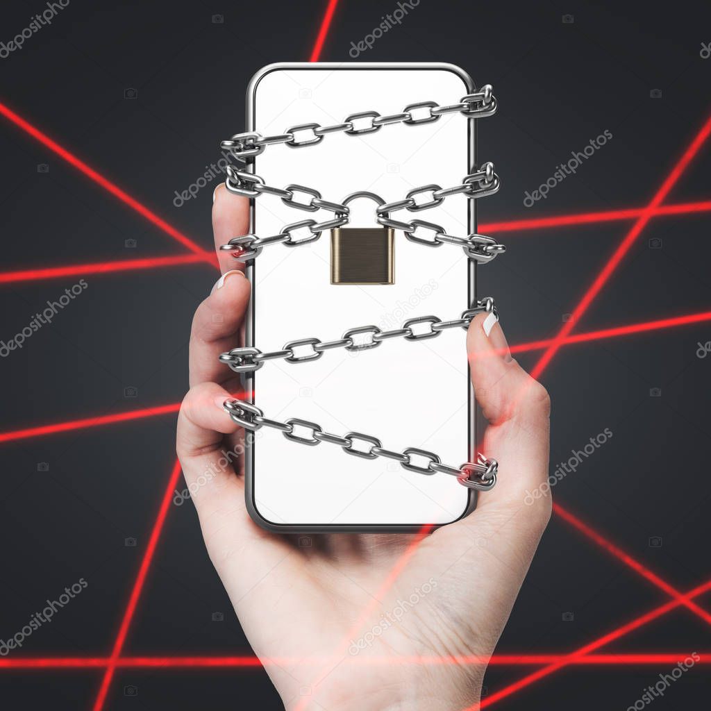 Hand of woman holding smartphone with chains and padlock on the screen over black background with laser rays. Digital security concept.