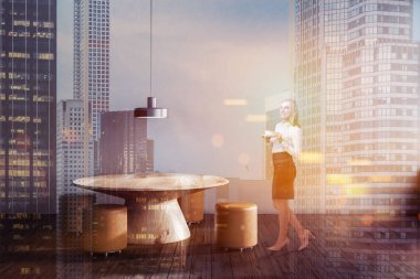 Gri duvar Restoran iç ahşap zemin, yuvarlak masa ve küçük kahverengi sandalye ile duran kadın. Çift tonlu görüntü pozlaması