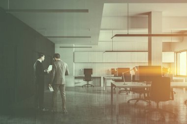 Açık alan office beyaz duvarlar, beton zemin, masaüstü bilgisayarlar ile bilgisayar tabloları satırları ile onlara konuşan iki iş adamları. Satır kapı duvar. Çift tonlu görüntü pozlaması