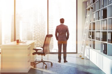 Çatı penceresi, beyaz masa dizüstü bilgisayar ve bir kitaplık ile ağıl ile ofisinde ayakta Yöneticisi. Tonlu görüntü