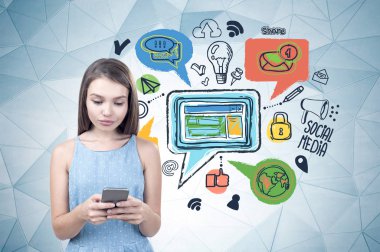 Genç kız ile renkli Sosyal Medya Icons üzerinde çizilmiş geometrik desen duvarının yakınında onu smartphone ekran ayakta bakarak mavi elbise.