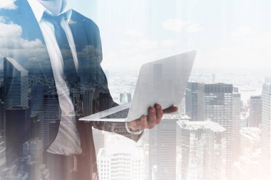 Tanınmayan işadamı koyu takım elbise ve modern cityscape arka plan üzerinde dizüstü bilgisayar ayakta tutan kravat takıyor. Çift Pozlama