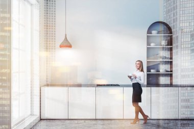 Sarışın kadın beyaz duvarlar, beton zemin, modern mutfak dolap ve beyaz mutfak tezgahı ile yapılı içinde tencere kemerli. Çift tonlu görüntü pozlaması