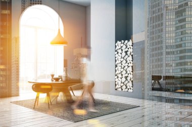 Kadın modern yemek odası ile gri duvarlar, ahşap zemin, köşesinde yuvarlak masa siyah sandalye ve bir şömine ile pencere kemerli. Tonlu görüntü çift pozlama bulanık