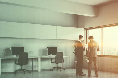 Modern ofis köşesinde beyaz duvarlar, beton zemin, satır ile masaüstü bilgisayar masalarının ile onları ve Saksı bitki köşedeki konuşurken işadamları. Çift tonlu görüntü pozlaması