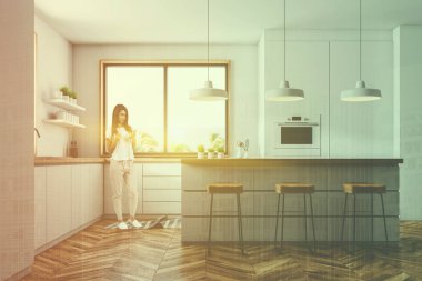 Kadın iç beyaz duvarlar, ahşap zemin, küçük bir pencere ile modern mutfak aletleri, bar tabureleri ile ve bir fırın beyaz mutfak tezgahı ile inşa. Çift tonlu görüntü pozlaması