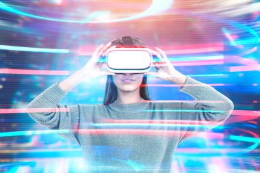 Genç kadın futuristik bir arayüze neon renkler ile ayakta kahverengi süveter ve vr gözlük takan uzun siyah saçlı. Çift tonlu görüntü pozlaması