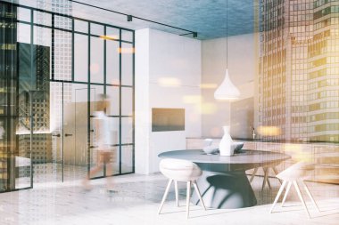 Kadın modern yemek odası ile bej duvarlar, ahşap zemin, köşesinde yuvarlak masa ahşap sandalye ile gri ve fırınlar içinde inşa. Tonlu görüntü çift pozlama bulanık