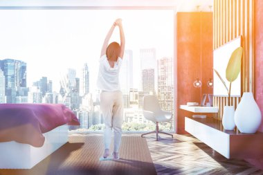 Yatak odası iç kırmızı duvarlar, ahşap zemin, panoramik penceresi, kırmızı ana yatak ve ev ofis köşe büyük tv seti ile kapatın. Kadın pijama. Tonlu görüntü