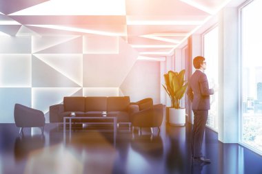 Ayakta beyaz geometrik desen duvarlar, siyah zemin ve siyah koltuk ve kanepe yakınındaki sehpa ile modern ofis bekleme odasında dostum. Tonlu görüntü