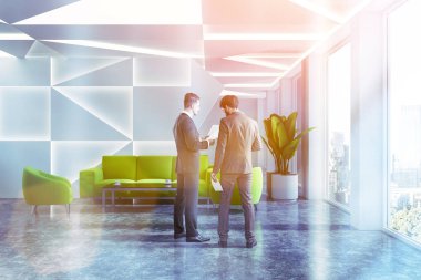 İşadamları beyaz geometrik ile modern ofis bekleme odasında duvarlar, beton zemin ve yeşil koltuk ve kanepe sehpa yakınındaki desen. Tonlu görüntü